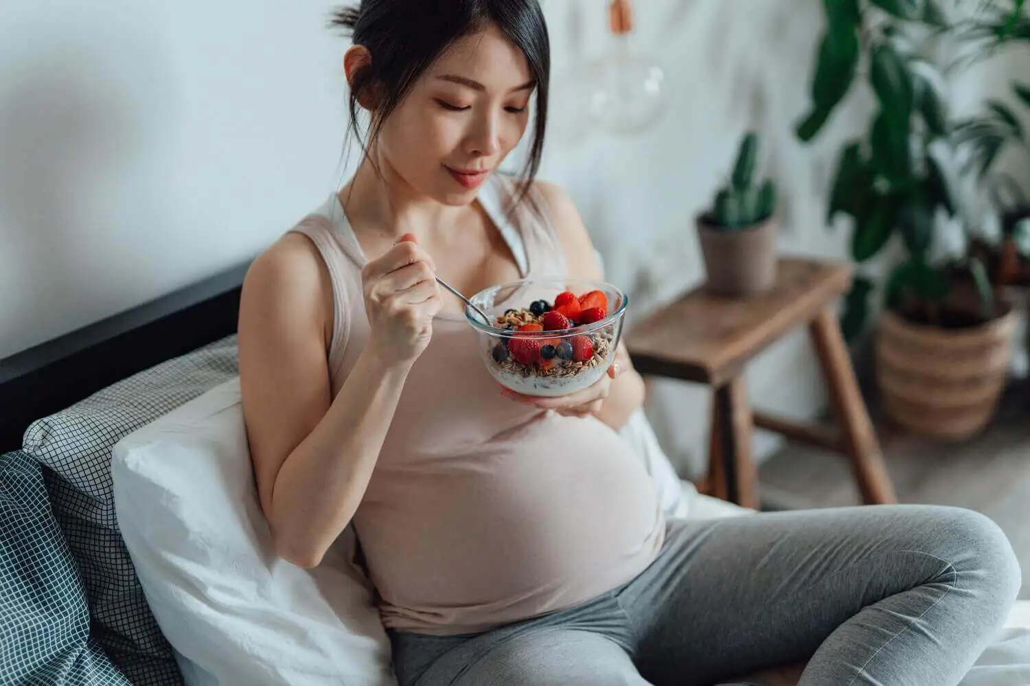 A pregnant woman enjoying a plate of berries and yogurt while sitting.
