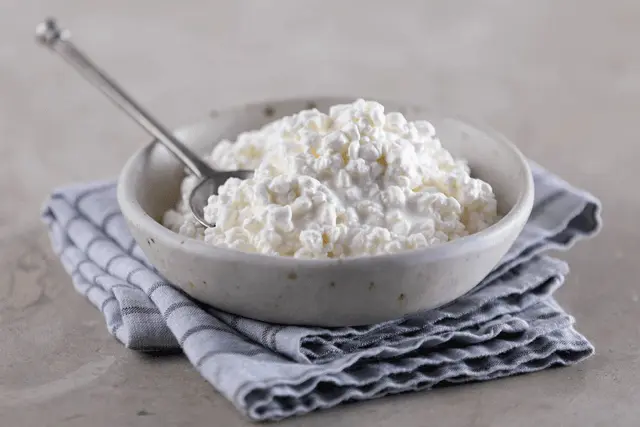 A stylish bowl filled with creamy cottage cheese, accompanied by a gleaming silver spoon.