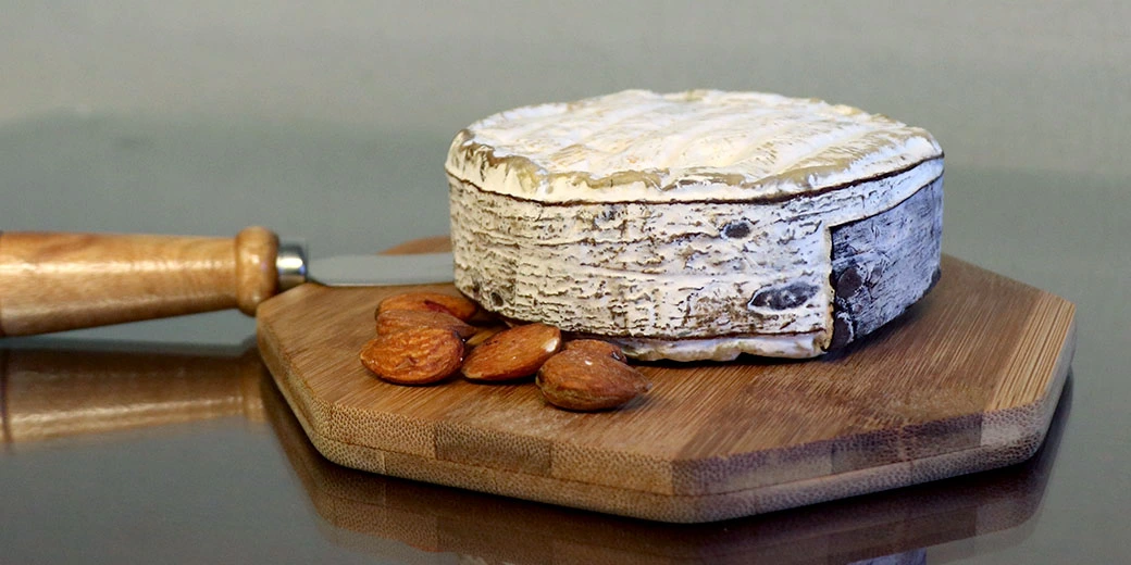A wheel of cheese with a bark rind being presented on a board with some almonds.