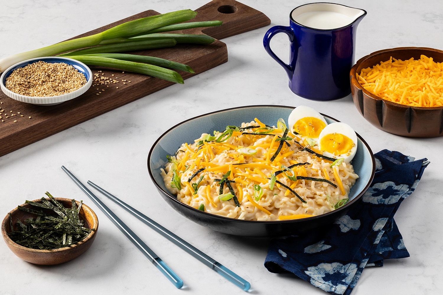 cheesy ramen noodles topped with cheddar cheese, green onions, sesame seeds, and nori with eggs on the side.