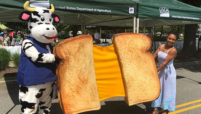 A person in a dairy cow costume and Olympian Dominique Dawes holding a giant cheese sandwich.